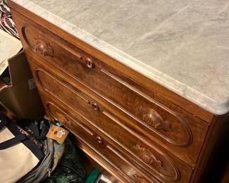 Marble Top Walnut Dresser — Solid walnut dresser with a white marble top and four carved drawers, stamped inside with maker's mark from Cincinnati. The piece features carved drawer fronts with original wooden knobs and a warm walnut finish that complements traditional or Victorian decor. Dimensions approximate a standard bedroom chest — see measurements below; heavy marble top adds stability but may require two people to move. Good overall condition with light surface wear, small scuffs and finish loss consistent with age; marble shows minor surface scratches but no major chips visible.