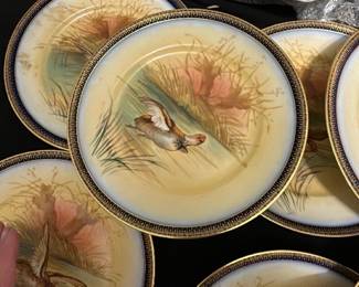 11-Limoges France Duck Plates — This lovely set of Limoges dinnerware from France features hand-painted ducks in a natural marsh scene, bordered with a rich cobalt and gold rim. The set includes 11 lunch size matching plates and 1 dessert dish, each crafted from fine porcelain with exquisite detail and vibrant colors. The plates measure approximately 9.5 inches in diameter, ideal for both display and dining. These plates are in good condition with minor signs of use and no visible chips or cracks. The backstamp confirms their authenticity as Limoges porcelain, a highly regarded maker known for quality French ceramics.