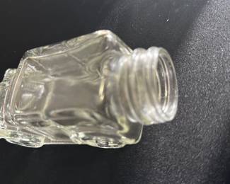 Vintage Glass Car Shaped Bottle — This vintage glass bottle is crafted in the shape of a classic car, featuring detailed embossed wheels and body contours. The clear glass construction highlights the charming automotive design, ideal as a collectible or decorative piece. The bottle measures approximately 4 in height, 2.5 in width, and 7 in length, making it a compact and eye-catching display item. It is in good condition with minor surface wear consistent with age and use. This unique car-shaped bottle adds character to any vintage collection or shelf display.