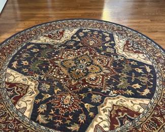 Paradise Blue Hand Made Wool Rug — This hand made wool rug from the Paradise collection by Mahdavi's A & A Ruy Co features a rich blue field with intricate traditional patterns. Crafted in India from quality wool, the carpet measures 7 feet 10 inches in diameter, showcasing detailed floral and geometric motifs that enhance any living room setting. The thick wool construction provides durability and softness underfoot, making it a beautiful and functional accent piece. The rug is in good condition with minor signs of wear consistent with use but no major damage. Originating from India, this piece highlights the craftsmanship of traditional woolen carpets.