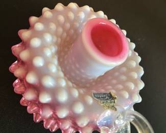 Fenton Cranberry Opalescent Candleholder — This lovely Fenton cranberry opalescent hobnail candleholder features a distinctive clear glass loop handle and a textured hobnail pattern for a vintage charm. Crafted from hand-blown glass with a white opalescent finish fading into cranberry, it serves as an elegant accent for any room. Measuring approximately 3 inches in height, 5 inches in width, and 4 inches in length, it is a perfect size for decorative use or collecting. The piece is in excellent condition showing no chips or cracks, retaining the original Fenton label that attests to its authenticity. This candleholder is a classic example of mid-20th century American art glass from the renowned Fenton Art Glass Company.