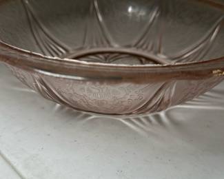 Pink Depression Glass Bowl — This delicate pink Depression glass bowl features classic pressed floral and geometric patterns that are emblematic of 1930s American glassware. Crafted from translucent pink glass, it has an elegant scalloped edge and a shallow, rounded form ideal for serving or decorative display. Measuring approximately 8 inches in diameter and 2.5 inches in height, this bowl is a charming example of vintage Depression glass collectibles. It is in good condition with some minor surface wear and a small chip on the rim consistent with vintage use. Perfect for collectors or as a vintage accent piece in any home décor.