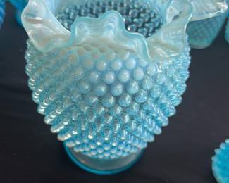 Blue Hobnail Vase with Ruffled Edge — This charming blue hobnail vase features a classic ruffled edge and textured body, characteristic of vintage hobnail glass designs. Made from opalescent glass, it showcases a beautiful gradient from blue to frosted white at the ruffled rim. The vase measures approximately 7 inches in height and 5 inches in width, making it an ideal decorative piece for a bedroom or living area. It is in good condition with no visible chips or cracks, showing minor surface wear consistent with age. This hobnail vase is a collectible piece that adds a touch of nostalgic charm to any collection or display.