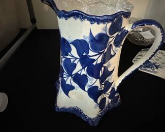 Blue White Floral Ceramic Pitcher — This charming ceramic pitcher features a blue floral leaf design on a white background, showcasing a unique scalloped rim and angular base. Hand-painted details highlight the classic style, while the sturdy handle offers ease of use. Measuring approximately 10 in height, 7 in width, and 5 in depth, this pitcher is perfect for decorative use or serving. It is in good condition with minor surface wear typical of vintage ceramics. The maker’s mark on the bottom reads: "Made by Mrs. Luis Davis, Independence."