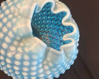 Blue Hobnail Milk Glass Vase — This charming blue hobnail milk glass vase features a striking ruffled edge and textured raised knobs around its rounded body. The vibrant blue color adds a vintage appeal, making it a perfect decorative accent for any room. It measures approximately 4 inches in height and 5 inches in width, ideal for small floral arrangements or as a stand-alone piece. The vase is in good condition with minor signs of wear typical for vintage glassware. Its classic hobnail design reflects mid-20th century glassmaking styles, perfect for collectors and enthusiasts.