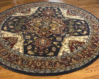 Paradise Blue Hand Made Wool Rug — This hand made wool rug from the Paradise collection by Mahdavi's A & A Ruy Co features a rich blue field with intricate traditional patterns. Crafted in India from quality wool, the carpet measures 7 feet 10 inches in diameter, showcasing detailed floral and geometric motifs that enhance any living room setting. The thick wool construction provides durability and softness underfoot, making it a beautiful and functional accent piece. The rug is in good condition with minor signs of wear consistent with use but no major damage. Originating from India, this piece highlights the craftsmanship of traditional woolen carpets.