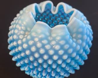 Blue Hobnail Milk Glass Vase — This charming blue hobnail milk glass vase features a striking ruffled edge and textured raised knobs around its rounded body. The vibrant blue color adds a vintage appeal, making it a perfect decorative accent for any room. It measures approximately 4 inches in height and 5 inches in width, ideal for small floral arrangements or as a stand-alone piece. The vase is in good condition with minor signs of wear typical for vintage glassware. Its classic hobnail design reflects mid-20th century glassmaking styles, perfect for collectors and enthusiasts.