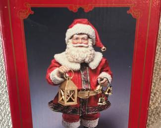 Holiday Traditions 10" Santa — Holiday Traditions 10" Fabric Mache Santa figure in original red box, perfect for seasonal mantel or tabletop display. The Santa wears a red fabric coat trimmed with white faux fur and carries a gold-tone lantern and bells; labeled as a 10-inch fabric mache construction. Boxed item from the Office Up Room; ideal for holiday decor and collectors of seasonal figures. Overall good condition with box showing light shelf wear and the figure appearing intact with no visible damage.