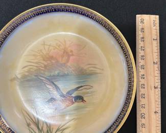 Limoges Hand-Painted Duck bowl — This beautiful Limoges plate features a hand-painted mallard duck in flight over a serene water scene. The plate has a deep blue and gold decorative border that enhances its classic elegance. Measuring approximately 10 inches in diameter, it is marked on the back with 'Limoges, France' and 'Lambides R&Co Paris.' The plate is in good condition with minor surface wear consistent with age and use. A stunning collectible from the renowned Limoges porcelain makers, perfect for display in any bedroom or dining collection.