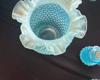 Blue Hobnail Vase with Ruffled Edge — This charming blue hobnail vase features a classic ruffled edge and textured body, characteristic of vintage hobnail glass designs. Made from opalescent glass, it showcases a beautiful gradient from blue to frosted white at the ruffled rim. The vase measures approximately 7 inches in height and 5 inches in width, making it an ideal decorative piece for a bedroom or living area. It is in good condition with no visible chips or cracks, showing minor surface wear consistent with age. This hobnail vase is a collectible piece that adds a touch of nostalgic charm to any collection or display.