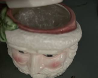 Ceramic Santa Cookie Jar — Charming ceramic Santa cookie jar with a removable hat lid, displayed in the blue dishes room. Hand-painted face with rosy cheeks, molded beard detail and holly accent on the hat; glazed finish shows light paint wear at the lid rim. Overall size is compact and countertop-friendly; holds a modest batch of cookies or candy. Good estate-condition with no obvious large chips or cracks visible in photos, minor rim paint loss noted.