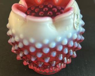 Fenton Cranberry Opalescent Hobnail Vase — This charming Fenton cranberry opalescent hobnail vase exhibits classic vintage glass artistry. The vase features a ruffled edge with a beautiful gradient from white opalescent to deep cranberry red adorned with a hobnail pattern for added texture. Measuring approximately 4 inches in height and 3 inches in diameter, it is a perfect decorative accent for any room. The piece is in excellent condition with the original Fenton label intact and no chips or cracks. A wonderful collectible that showcases Fenton's timeless hand-crafted glass tradition.