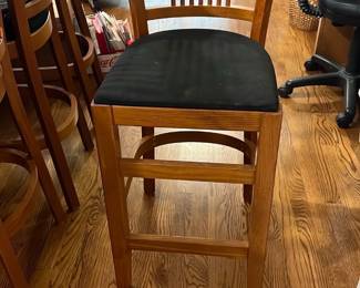 Wooden Counter Height Bar Stool — This wooden counter height bar stool features a classic design with vertical slat backrest and a black cushioned seat. Crafted from polished wood, it offers sturdy construction suitable for kitchen or bar use. The stool measures approximately 43 inches in height, 17 inches in width, and 17 inches in depth, providing comfortable seating at standard counters. It is in good condition with minor signs of use on the cushion but structurally sound. Its simple, timeless design blends well with various home decor styles.