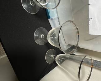 Crystal Lotus Glassware Set — This crystal Lotus glassware set includes tea glasses, water glasses, and sherbet glasses as indicated by the seller's notes. The collection features delicate stems and clear bowl shapes suitable for various drinks, making it an elegant addition to any table setting. There are 8 tea glasses, 8 water glasses, and 7 sherbet glasses stored in a labeled plastic container in the bonus up room. The glasses appear to be in good condition with no visible chips or cracks. Perfect for formal dining or special occasions.