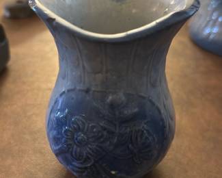 Blue Floral Ceramic Vase — This charming blue ceramic vase features an embossed floral pattern with intricate details. Its unique flared and scalloped rim adds character to this decorative piece, ideal for dining room display or flower arrangements. The vase measures approximately 5 in height and 3.5 in width, making it a perfect accent for small spaces. It is in good condition with minor surface wear consistent with age but no visible chips or cracks. A lovely example of vintage home decor suitable for collectors or daily use.