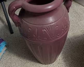 Pink Two-Handled Ceramic Urn — Large pink two-handled ceramic urn with neoclassical relief decoration and a wide flared rim. The piece features molded shell and foliate motifs around the shoulder and vertical fluting on the body; maker's marks and numbers are incised on the base (visible in photos). Approximately 24 inches tall and sturdy enough for floor display or use as an umbrella/plant holder in a bonus up room. Overall good condition with surface scuffs and small chips consistent with normal use; base shows manufacturing marks and handwriting. A decorative statement piece suitable for entryway or living room display.