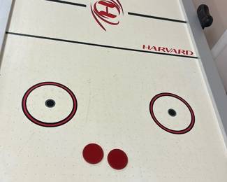 Harvard Air Hockey Table — This Harvard air hockey table combines classic arcade fun with durable construction and a sleek design. It features a white play surface with red and black markings, including the Harvard logo and name prominently displayed on both ends and center ice. The table measures approximately 84 inches in length, 42 inches in width, and 30 inches in height, making it suitable for home game rooms or recreational spaces. In good condition, it shows minor signs of use with clean playing surface and intact legs providing sturdy support. Ideal for entertaining family and friends in a basement or game room setting.