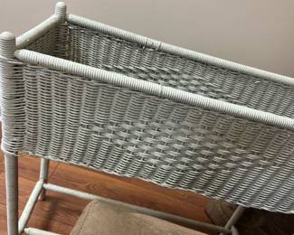 White Wicker Planter Stand — This white wicker planter stand features a woven basket design elevated on four sturdy legs. Crafted for indoor use, it provides an elegant way to display plants or organize items while adding a touch of vintage charm. Measuring approximately 23 inches tall, 18 inches wide, and 10 inches deep, it fits comfortably in small spaces such as basement rooms or sunrooms. The wicker shows minor wear and some unraveling but remains structurally sound. Ideal for adding character to home decor, this piece balances utility with classic woven craftsmanship.