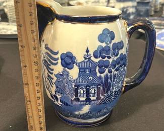 Buffalo Pottery Blue White Pitcher — This charming Buffalo Pottery pitcher features a classic blue and white design with a scenic pagoda and tree motif. Crafted from fine pottery and marked on the bottom with a Buffalo Pottery 1908 stamp, it measures approximately 7.5 inches tall. The pitcher is in good condition with light wear consistent with age and use. It is a timeless piece suited for collectors of vintage American pottery or those appreciating early 20th-century design.