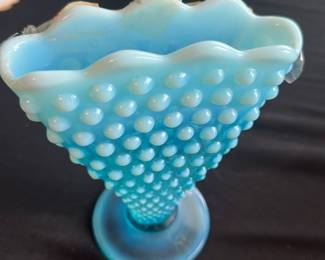 Fenton Blue Hobnail Opalescent Vase — This charming Fenton blue hobnail opalescent vase stands 6 inches tall and features a distinctive hobnail pattern with a flared, ruffled rim. Crafted with opalescent glass, this vintage piece adds a delicate and collectible touch to any room. The vase measures approximately 6 inches in height and has a stable round base. It is in good condition with no visible chips or cracks, though some minor surface wear may be present consistent with age. A classic example of Fenton's artisan glasswork, perfect for collectors or vintage decor enthusiasts.