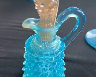 Fenton Blue Hobnail Cruet — This charming Fenton blue hobnail cruet features a classic antique design with raised hobnail glass texture. Made of vibrant blue opaque glass, it includes a matching stopper with a hobnail pattern. Measuring approximately 5 inches in height and 3 inches in width, this piece adds a touch of vintage elegance to any collection. It is in good condition with no visible chips or cracks. A lovely example of early to mid-20th century American glassware.