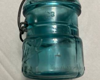 Ball Aqua Glass Jar with Wire Bale — This vintage Ball glass jar features a distinctive aqua blue color and a wire bale closure, typical of early 20th-century canning jars. Made from thick glass, it includes embossed Ball branding and a patent date indicating its collectible nature. Measuring approximately 4 inches in height and 3 inches in diameter, it is a sturdy piece suitable for display or storage. The jar is in good condition with signs of use and some minor wear to the wire bale closure. A great addition for collectors of vintage kitchenware or rustic home decor.