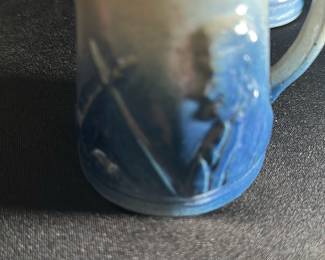 Blue Ceramic Vintage Creamer Pitcher — This vintage ceramic creamer pitcher features a charming blue glaze with embossed rustic designs including a windmill and cottage scene. The pitcher offers a classic form with a graceful spout and comfortable handle, ideal for serving cream or milk. Measuring approximately 3.5 inches tall and 3 inches wide, it is compact and perfect for tabletop use or display in a collection. The piece is in good condition with minor wear consistent with age but no visible chips or cracks. The pottery's rustic design and blue glazed finish make it a distinctive addition to vintage ceramic collections.