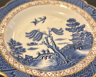 Blue Willow real old willow  Plate — This charming Soothe 'Real Old Willow' scalloped plate from England showcases classic blue and white Willow pattern imagery with gold trim. Crafted from fine ceramic, it features a detailed bridge, willow tree, and pagoda scene in blue hues against a white base accented by an intricate border design. The plate measures approximately 9.5 inches in diameter, making it suitable for display or dining use. It is in good condition with minor surface discoloration noted but no chips or cracks visible. A lovely example of traditional English transferware from a respected maker.