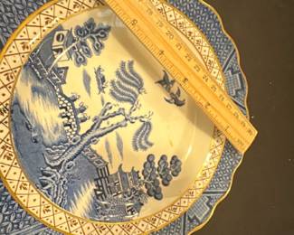 Blue Willow real old willow  Plate — This charming Soothe 'Real Old Willow' scalloped plate from England showcases classic blue and white Willow pattern imagery with gold trim. Crafted from fine ceramic, it features a detailed bridge, willow tree, and pagoda scene in blue hues against a white base accented by an intricate border design. The plate measures approximately 9.5 inches in diameter, making it suitable for display or dining use. It is in good condition with minor surface discoloration noted but no chips or cracks visible. A lovely example of traditional English transferware from a respected maker.