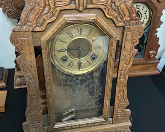 Antique Carved Wood Mantel Clock — This antique mantel clock features an intricately carved wooden case adorned with detailed lion figures and ornamental floral designs. The clock face displays Roman numerals and is protected by a glass door with etched decorative elements. Measuring approximately 18 inches tall, 12 inches wide, and 5 inches deep, this clock is a standout piece for any vintage collection or classic home decor. The clock shows signs of age with a patina on the dial and some wear on the wood, but overall remains structurally sound. Its detailed craftsmanship and majestic lion motifs suggest a late 19th to early 20th-century origin, offering timeless elegance to any room.