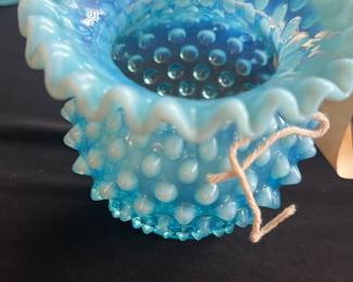 Fenton Blue Opalescent Hobnail Vase — This charming Fenton hobnail vase features a stunning blue opalescent glass with a ruffled edge, characteristic of mid-20th century American art glass. The hobnail pattern enhances its textured beauty and classic collectible appeal. Measuring approximately 4.5 inches in height and 4 inches in width, this vase is perfect for display or small floral arrangements. It is in excellent condition with no chips or cracks visible. A delightful piece for collectors of vintage Fenton glassware.
