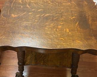 Oak End Table with Claw Feet — This charming oak end table features a scalloped top and a lower shelf for added storage or display. The table is supported by intricately turned legs ending in distinctive claw feet, adding a vintage touch. Measuring approximately 26 inches high, 28 inches wide, and 20 inches deep, it fits well in various living spaces. The piece is in good condition with minor surface wear consistent with age, preserving its character and sturdy construction. Ideal for use as a side table or accent piece in traditional or rustic decor.