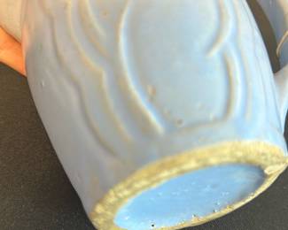 Vintage Blue Pottery Creamer Pitcher — This charming vintage creamer pitcher features a soft blue glaze with embossed decorative swirls, giving it a subtle yet elegant look. Crafted from ceramic pottery, the piece displays an artisan handmade quality with a comfortable handle and a functional pour spout. Measuring approximately 3.5 inches in height, 4.5 inches in width including the handle, and 2.5 inches in depth, it's well-suited for use in the master bedroom or as a decorative collectible. It is in good condition with small imperfections consistent with vintage handmade pottery. This pitcher adds a delicate, classic touch to any table setting or display collection.