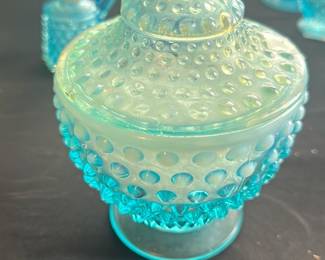 Hobnail Blue Glass Covered Bowl — This charming hobnail blue glass covered bowl features a textured design with raised bumps all around the body and lid, topped with a decorative finial. The translucent aqua blue color gives it a vintage and decorative appeal, perfect for display or serving small treats. It measures approximately 7.5 inches tall and 6 inches wide, making it a compact yet striking collector's piece. The bowl is in good condition with no visible chips or cracks, preserving its nostalgic charm. Ideal for vintage glassware collectors or elegant home decor accent.