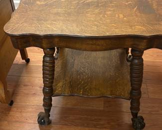 Oak End Table with Claw Feet — This charming oak end table features a scalloped top and a lower shelf for added storage or display. The table is supported by intricately turned legs ending in distinctive claw feet, adding a vintage touch. Measuring approximately 26 inches high, 28 inches wide, and 20 inches deep, it fits well in various living spaces. The piece is in good condition with minor surface wear consistent with age, preserving its character and sturdy construction. Ideal for use as a side table or accent piece in traditional or rustic decor.