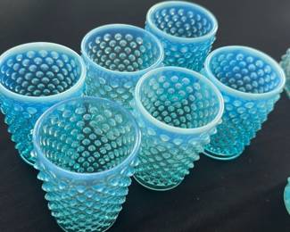 Blue Hobnail Glass Tumbler Set — This charming set includes six blue hobnail glass tumblers, perfect for adding a vintage touch to your drinkware collection. Each tumbler features raised hobnail patterns over frosted blue glass, typical of mid-century decorative glassware. The tumblers measure approximately 4.5 inches in height with a 3-inch diameter, making them ideal for serving cocktails or water. These glasses are in good condition with no visible chips or cracks, showcasing their sturdy vintage craftsmanship. Their vibrant blue color and textured design make them a standout addition to any table setting or glass collection.