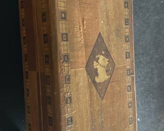 Vintage Wooden Inlay Jewelry Box — This vintage wooden jewelry box features intricate inlay work with a geometric border and a central motif of a dog figure. Constructed from wood with a hinged lid, the box is divided internally into two compartments, ideal for organizing small items. Measuring approximately 7 inches in length, 4 inches in width, and 3 inches in height, it offers a compact storage solution with a charming rustic appearance. The box shows some wear consistent with vintage use, adding to its character without compromising its integrity. Perfect for collectors of unique wooden boxes or vintage home decor items.