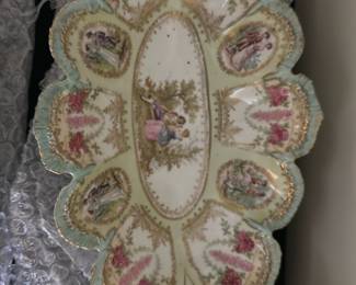 RS Russia Relish Dish Blue Pink Gold — This RS Russia relish dish showcases exquisite craftsmanship with delicate blue, pink, and gold accents. The dish features ornate scalloped edges with intricate floral gold detailing and romantic Victorian-style figures in various oval sections. Measuring approximately 12 inches in length and 8 inches wide, this porcelain piece is decorative and perfect for special occasions or display. It is in good condition with minor wear consistent with age but no visible chips or cracks. The RS Russia maker's mark is present on the bottom, confirming its authenticity and collectible value.