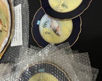10Limoges France Blue Fish Plates Set — This set of 10 Limoges France plates features a distinctive dark blue border with gold trim and a detailed hand-painted fish design in the center. Crafted from fine porcelain, these collectible plates combine traditional artistry with elegant decoration, making them perfect for decorative or functional use. Each plate measures approximately 10.5 inches in diameter, ideal for display or serving. The plates are in good condition with no visible chips or cracks, showcasing their enduring quality. A beautiful example of Limoges craftsmanship, these plates add a classic touch to any collection or dining setting.