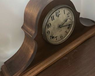 Gilbert Vintage Wooden Mantel Clock — This charming Gilbert vintage wooden mantel clock features a classic tambour style with smooth curved edges. The clock face shows aged patina with bold black numerals and the Gilbert brand mark visible. Measuring approximately 9 inches tall, 17 inches wide, and 5 inches deep, this clock is designed for display on a mantel or shelf. The wood casing exhibits some wear consistent with age but remains structurally sound. A fine example of early 20th-century American clockmaking, it adds vintage character to any room.
