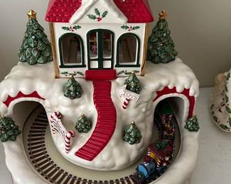Lenox Santa's Workshop “Toyland” — This festive Holiday Santa's Workshop Centerpiece captures the charm of a snow-covered Christmas village with detailed red roofs, holly accents, and festive trees. The ceramic piece features a circular train track with a colorful toy train, surrounded by candy cane signs and wrapped presents, perfect for holiday décor. Measuring approximately 8 inches tall and 10 inches wide, it is a delightful and eye-catching addition to any holiday setting. The item is in excellent condition with no visible chips or cracks. Its classic holiday theme makes it ideal as a centerpiece or collector's piece for Christmas enthusiasts.