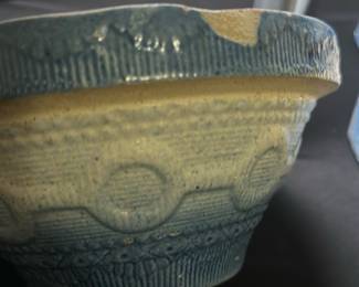 Blue Patterned Pottery Bowl — This blue-patterned pottery bowl features a textured design with circular and linear motifs along the exterior rim and body. The bowl has a cream-colored interior and subtle rustic detailing on the base. Measuring approximately 3.5 inches tall and 7.5 inches in diameter, it is a charming decorative or functional piece. There is a visible chip on the rim and some wear on the base consistent with age and use, adding character to the bowl. Its handmade look and glaze suggest a vintage or artisan origin, suitable for collectors or casual display.