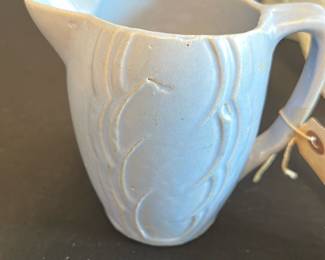 Vintage Blue Pottery Creamer Pitcher — This charming vintage creamer pitcher features a soft blue glaze with embossed decorative swirls, giving it a subtle yet elegant look. Crafted from ceramic pottery, the piece displays an artisan handmade quality with a comfortable handle and a functional pour spout. Measuring approximately 3.5 inches in height, 4.5 inches in width including the handle, and 2.5 inches in depth, it's well-suited for use in the master bedroom or as a decorative collectible. It is in good condition with small imperfections consistent with vintage handmade pottery. This pitcher adds a delicate, classic touch to any table setting or display collection.