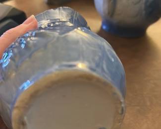 Blue Floral Pottery Pitcher — This charming blue floral pottery pitcher features an intricate embossed flower design on its exterior. The piece has a gracefully flared rim and sturdy handle, ideal for decorative or functional use in the dining room. It measures approximately 5.5 inches in height, 3.5 inches in width, and 4 inches in length, making it a compact yet elegant addition. The pitcher is in good condition, showing some wear consistent with age but no significant damage. Its classic style and glazing suggest it would complement vintage or home decor collections.