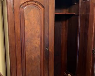 Antique Mahogany Wardrobe Cabinet — This vintage mahogany wardrobe cabinet features classic solid wood construction with beautiful grain patterns and ornate panel doors. It includes a hanging shelf inside and a spacious lower drawer with decorative brass handles, offering ample storage for clothing or linens. The cabinet measures approximately 87 in height, 50 in width, and 22 in depth, making it suitable for bedroom or dressing room use. The condition is good with minor wear consistent with age, showing some patina but no structural damage. Its traditional design and quality craftsmanship make it a timeless storage piece.
