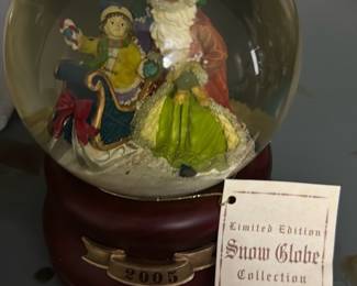 Limited Edition Snow Globe 2005 — Limited Edition Snow Globe Collection globe dated 2005 featuring a Santa figure with a child in a sled on a wooden-tone base. The globe is glass with hand-painted resin figures and a maroon-colored base plate with a 2005 brass plaque; original tag from the series is included. Measures approximately 6 in tall with a 4.5 in diameter globe (overall dimensions estimated) and is a lightweight tabletop holiday piece. Good condition with light surface wear to base and intact glass; mechanism on the bottom appears complete though functionality (music/wind-up) not tested.