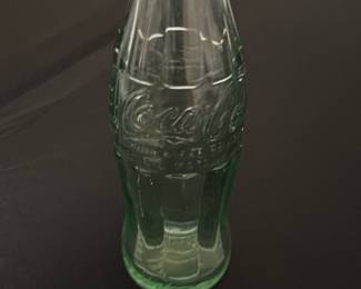 Vintage Coca-Cola Miniature Glass Bottle — This vintage Coca-Cola miniature glass bottle is a collectible piece showcasing the iconic contoured design and embossed logo. Made from green-tinted glass, it represents classic Coca-Cola branding and style from mid-20th century memorabilia. The bottle measures approximately 4.25 inches in height and 1.5 inches in width, perfect for display in any collection or as a decorative accent. It is in good condition with some light surface wear typical for its age. A charming collectible for enthusiasts and vintage glassware collectors.