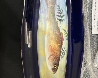 Limpges France Cobalt Blue Fish Platter — This Limpges France fish platter features a striking hand-painted fish design against a cobalt blue background. Crafted from fine porcelain, it showcases intricate naturalistic details and delicate gold trim accents on its ornate edges. Measuring approximately 18 inches in length and 7 inches in width, this platter is perfect for serving or display. It is in excellent condition with no visible chips or cracks, reflecting high-quality craftsmanship. A beautiful example of French porcelain artistry, ideal for collectors or as a decorative piece.