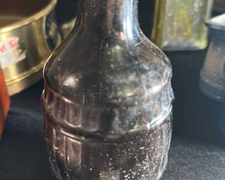 Vintage Glass Bottle — This vintage black glass bottle features a distinct rounded, ribbed design reminiscent of early 20th century glassware. Its compact size and textured surface suggest it may have been used for medicinal or decorative purposes. Measuring approximately 4.5 inches in height and 2.5 inches in width, this bottle is a charming collectible for vintage glass enthusiasts. The bottle shows signs of age with some surface speckling and minor wear but is structurally intact. It makes a great addition to any collection of antique or vintage bottles.