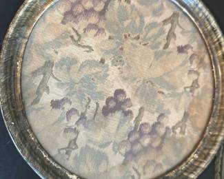 Vintage Metal Tray with Fabric Insert — This vintage metal tray features a round design with a fabric insert displaying a delicate grapevine pattern in muted purple and green tones. The tray has two handles for easy carrying and exhibits a rustic patina that enhances its antique charm. Measuring approximately 17 inches in diameter with a shallow depth, it is an excellent decorative or serving piece. The tray shows signs of wear consistent with age but remains structurally sound. Ideal for vintage collectors or as a unique home decor accent.